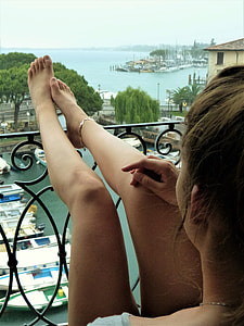woman wearing grey top raising her feet on black metal fence under white sky during daytime thumbnail