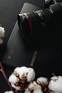 black Canon DSLR camera with zoom lens on black Samsung Chromebook laptop thumbnail