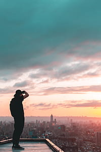 man standing on rooftop looking in city buildings during golden hour thumbnail