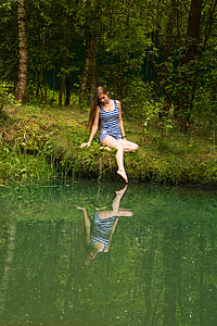woman wearing blue and white striped tank top sitting on grass near calm body of water thumbnail