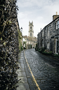 concrete road between buildings with clock tower on far distance under gray sky during daytime thumbnail
