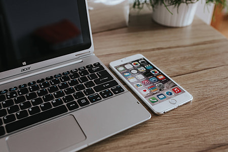 Silver Acer laptop, a white Apple iPhone and a notepad on a wooden desk thumbnail