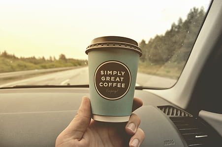 person holding gray and brown disposable coffee cup inside vehicle during daytime thumbnail