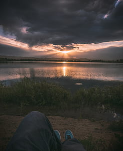 person reclining near body of water with crepuscular rays thumbnail