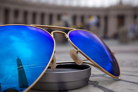 selective focus photo of blue lens Aviator-style sunglasses with gold-colored frames on round gray case thumbnail