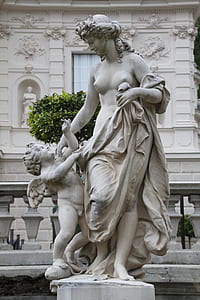 naked woman and cherub statue in front of white building thumbnail