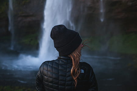 woman in black knit cap standing in front waterfalls thumbnail
