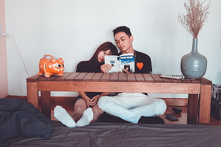 Couple Reading Book Sitting on Front of Rectangular Brown Wooden Coffee Table thumbnail