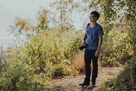 man standing outdoors with black DSLR camera sling on his right shoulder thumbnail