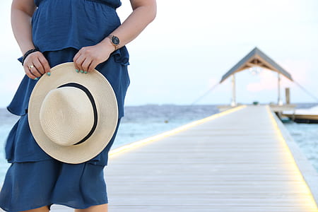 woman holding white sun hat while standing on dock during day thumbnail