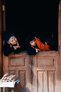 woman and two child leaning on brown wooden door looking sideways at daytime thumbnail