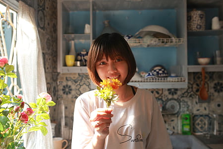 smiling woman holding yellow and orange petaled flowers thumbnail