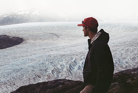 man standing on mountain peak facing snow plains thumbnail
