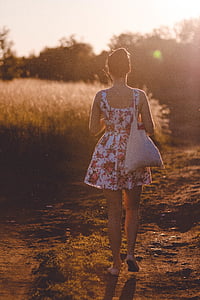 woman walking on dirt road during golden hour thumbnail