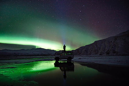 person standing on top of white SUV near mountain ridges watching Northern Lights thumbnail