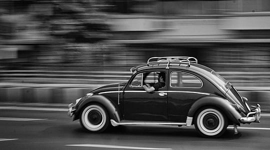 grayscale photo of man riding on beetle car on road thumbnail
