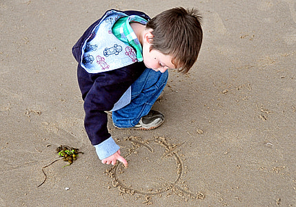 boy drawing through sand wearing purple jacket thumbnail