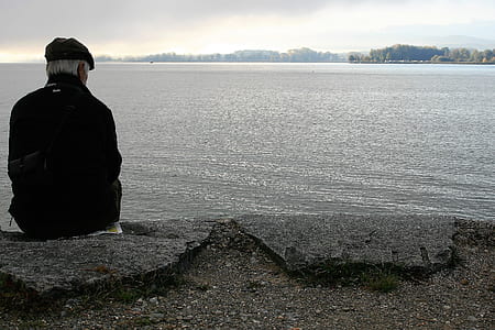 man sitting on concrete platform near body of ocean thumbnail