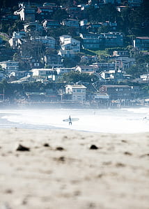 person walking on seashore carrying surfboard thumbnail