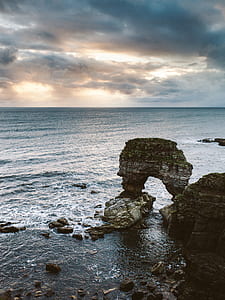 gray rock formation surround by sea under white and blue cloudy sky thumbnail