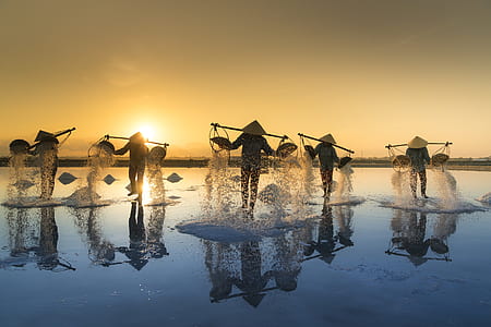 silhouette five men wearing hats carrying over-shoulder baskets on water during golden hour thumbnail
