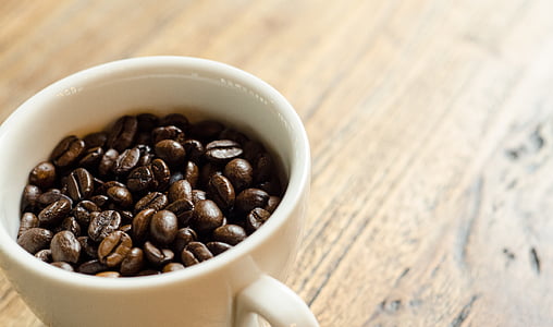 white ceramic coffee mug with coffee beans on top of brow wooden surface thumbnail
