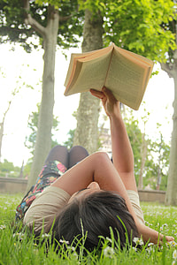 woman lying on grass field reading book beside green tree thumbnail