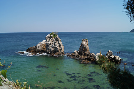 gray rock formation in body of water under blue sky during daytime thumbnail