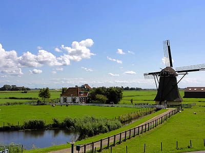 windmill and near house on grass lawn under blue and white cloudy sky thumbnail
