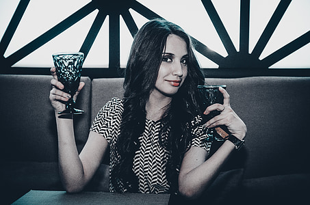 woman sitting on gray sofa while holding two black glass goblets thumbnail