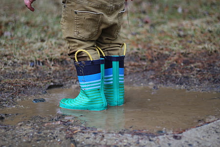 person with brown denim pants tea-and-black rain boots on body of water during daytime thumbnail