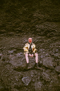 Man Wearing Gold Jacket Sitting on Stone thumbnail