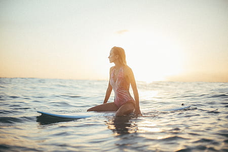 woman wearing red and white monokini sitting on blue surfboard on sea during sunset thumbnail