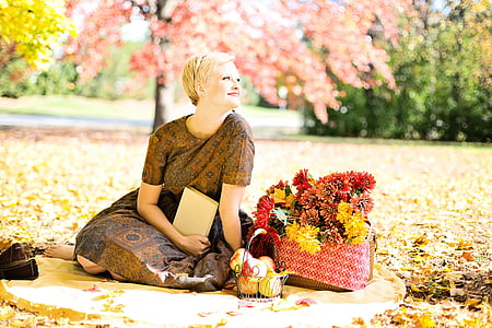 woman wearing brown floral dress sitting beside basket of red and yellow petaled flowers thumbnail