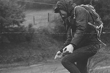 grayscale photo of person in hoodie near trees thumbnail