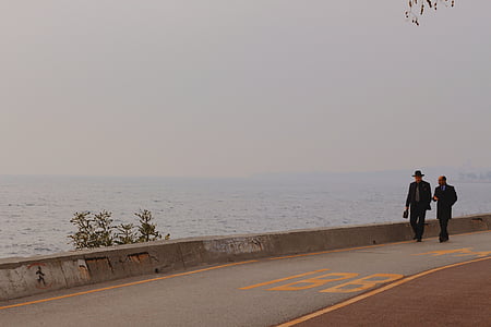 two person walking on the side of the road near body of water thumbnail
