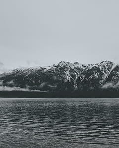 greyscale photo of body of water and mountain thumbnail