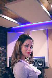 woman in gray shirt standing inside studio while smiling thumbnail