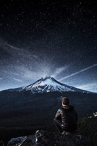 man sitting on rock while looking at mountain alps at night thumbnail