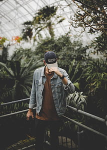 man holding cap while standing beside gray metal fence thumbnail