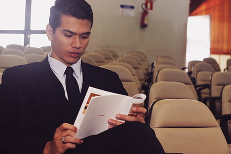 man sitting on brown padded chair reading book thumbnail