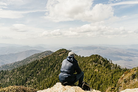 person sitting on rock facing mountain ranges thumbnail