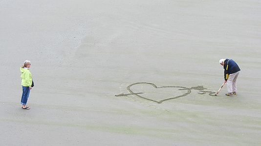 man creating heart with arrow in sand during daytime thumbnail