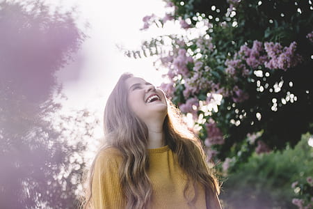 laughing woman surrounded by pink flowers and trees during daytime thumbnail