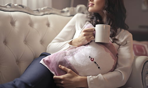 A young brunette woman sitting on the couch holding a coffee mug in her hand in the living room thumbnail