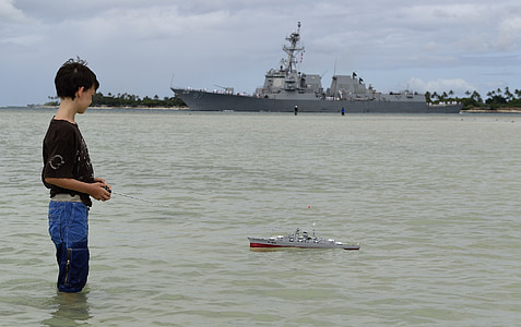 boy standing on sea playing toy ship thumbnail