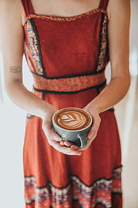 person in orange dress holding cup of coffee art latte thumbnail