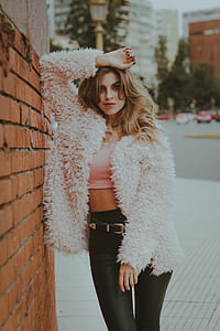 woman wearing white coat leaning on brown wall thumbnail