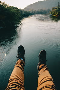 Man in Black Sneakers And Brown Pants Sitting in Front of the River thumbnail