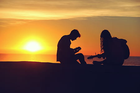 silhouette of two people holding string instruments during sunset thumbnail